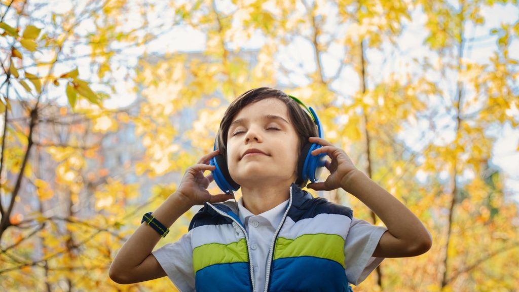 Jongentje luistert in de buitenlucht met z'n ogen dicht naar muziek op zijn blauwe koptelefoon