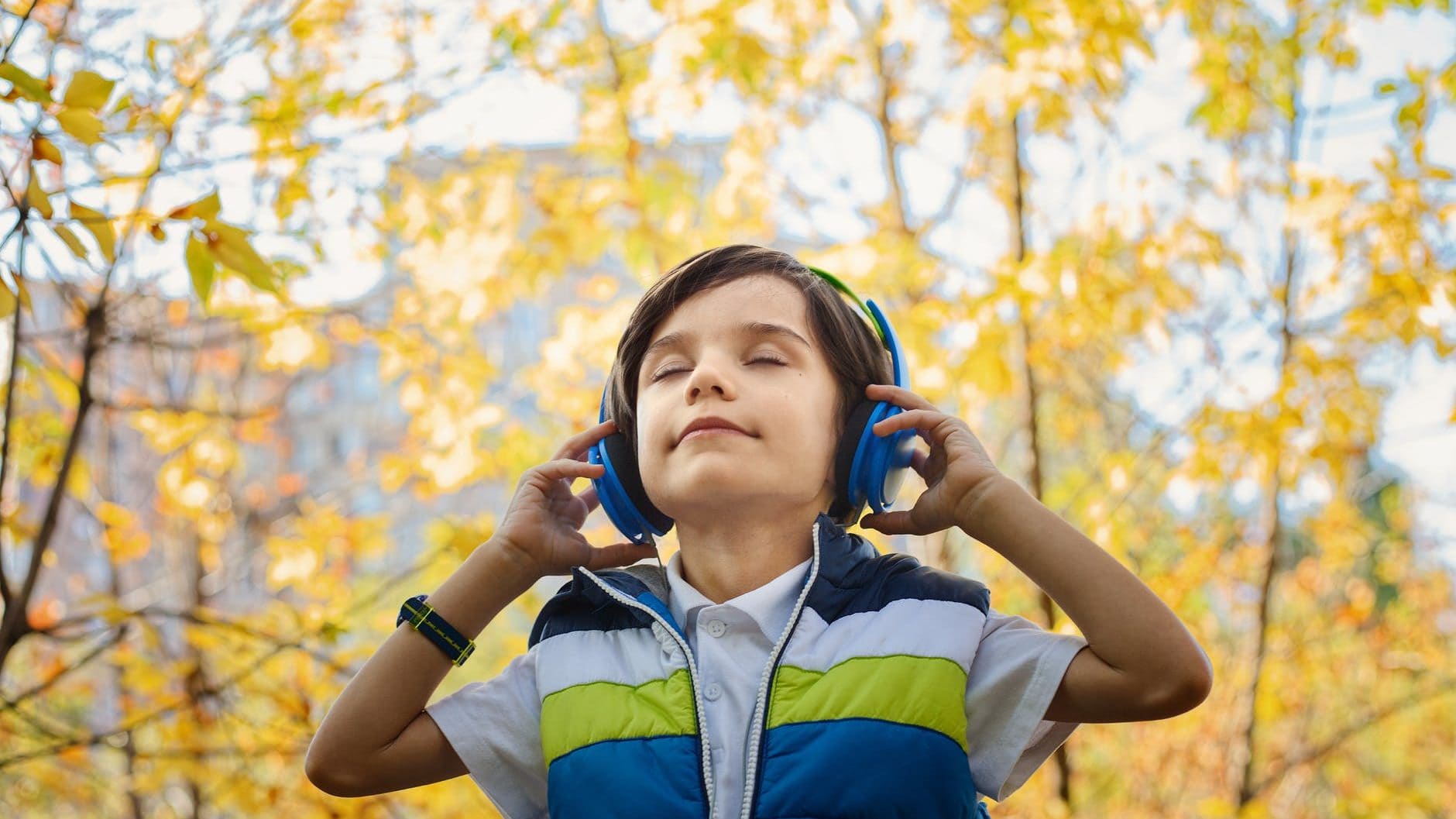 Jongetje staat in de natuur te genieten van de muziek met zijn koptelefoon op.