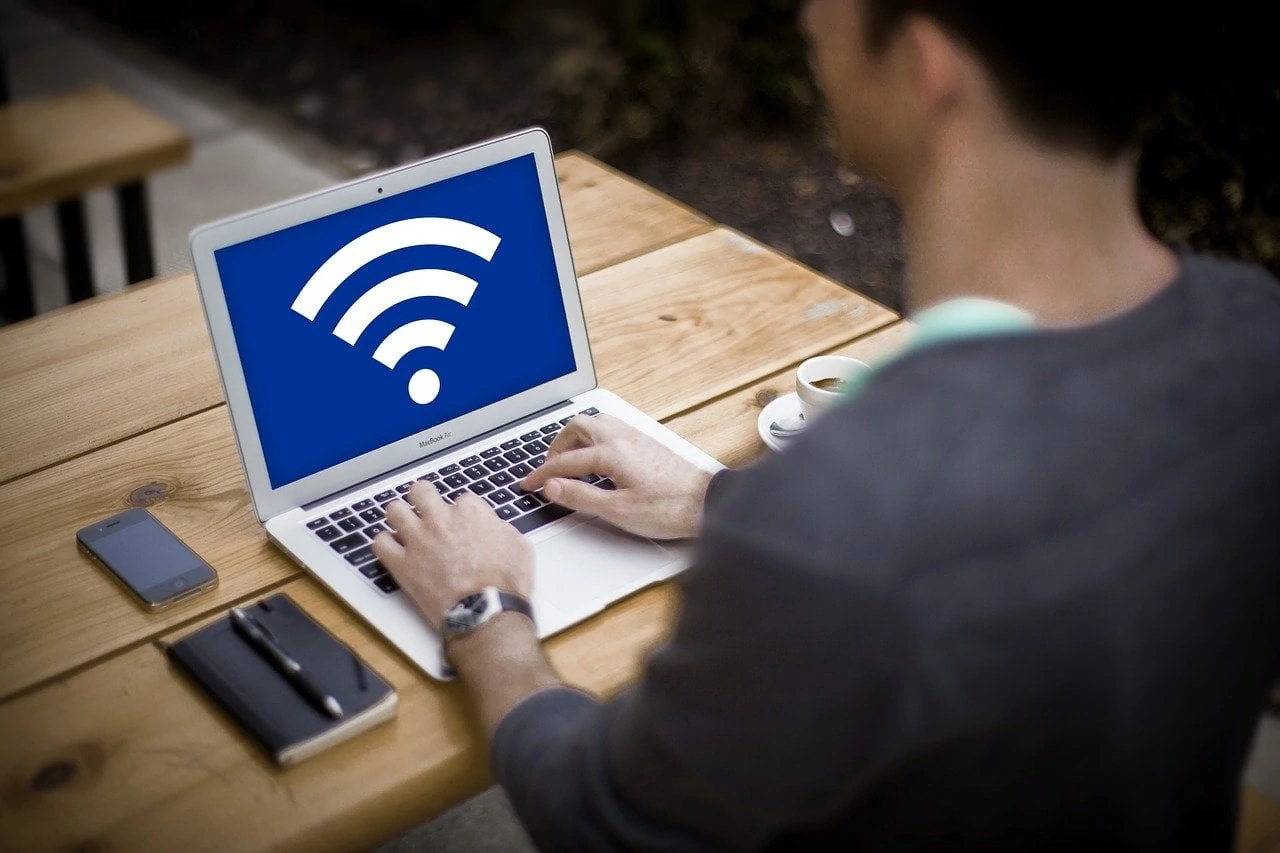 man zit aan tafel achter laptop met wifi-logo op het scherm