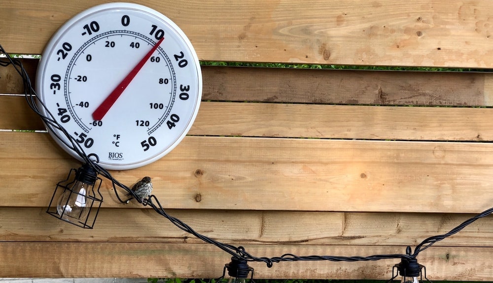 wandthermometer die omgevingstemperatuur weergeeft op hek in achtertuin met lampjes eronder
