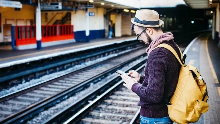 Man wacht op zijn trein met smartphone in de hand