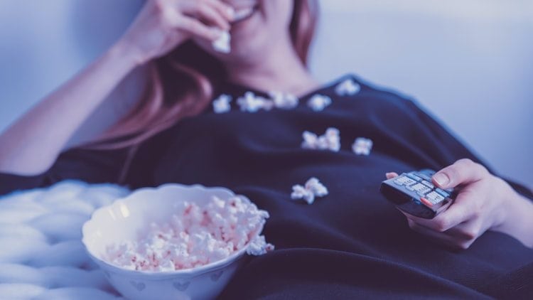 Vrouw eet popcorn met een afstandsbediening in haar hand