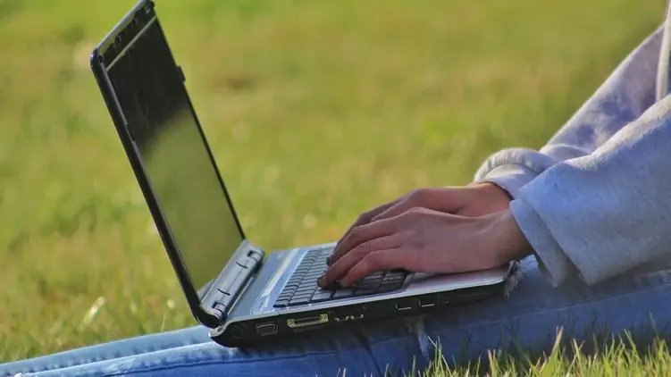Vrouw werkt in het gras met haar laptop