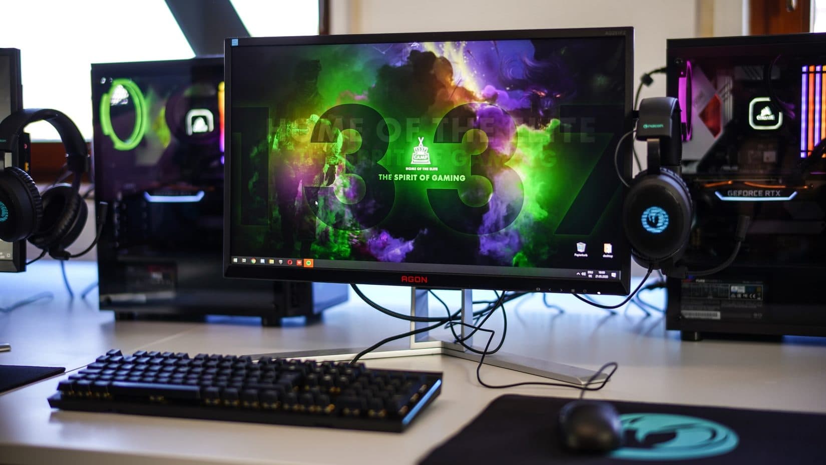 Gaming monitor naast twee gaming pc's met toetsenbord, muis en koptelefoons