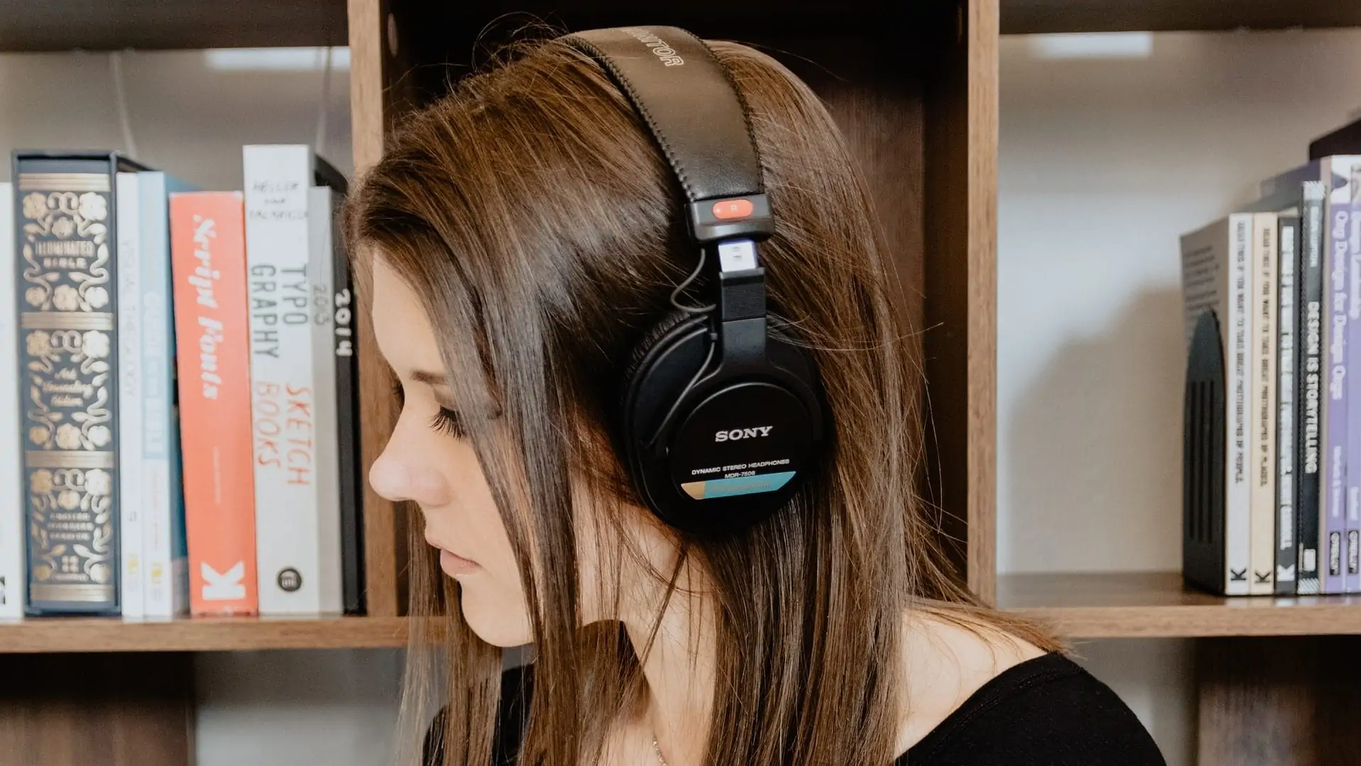 Vrouw met over-ear headset op, voor een boekenkast