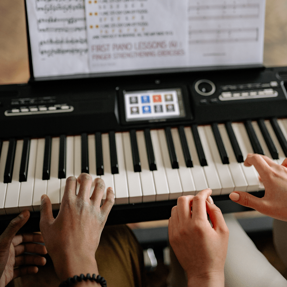 Twee personen bespelen samen een digitale piano