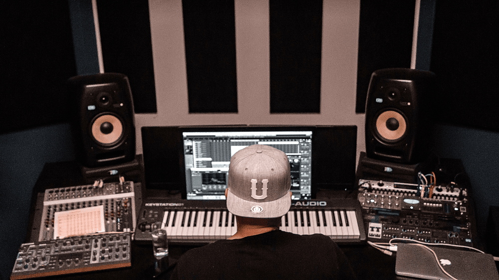 Een muziekproducent die voor zijn piano zit met twee studio monitoren