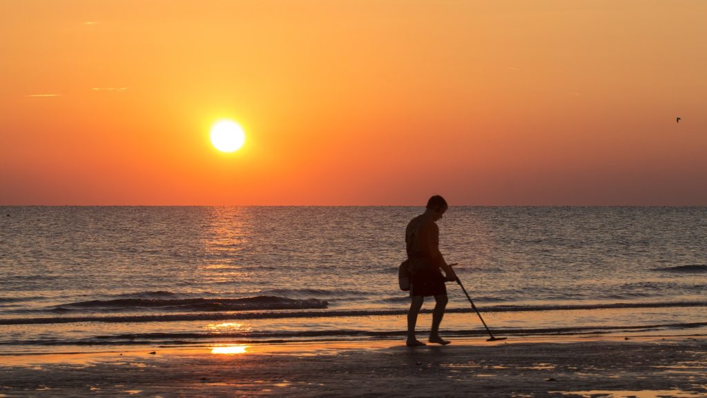 Een man is op zoek naar verborgen spullen op het strand met een metaaldetector