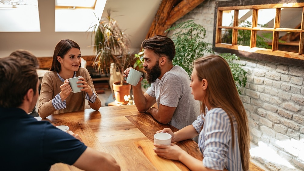 Vier vrienden in een landelijke woonkamer zitten aan tafel en drinken samen koffie