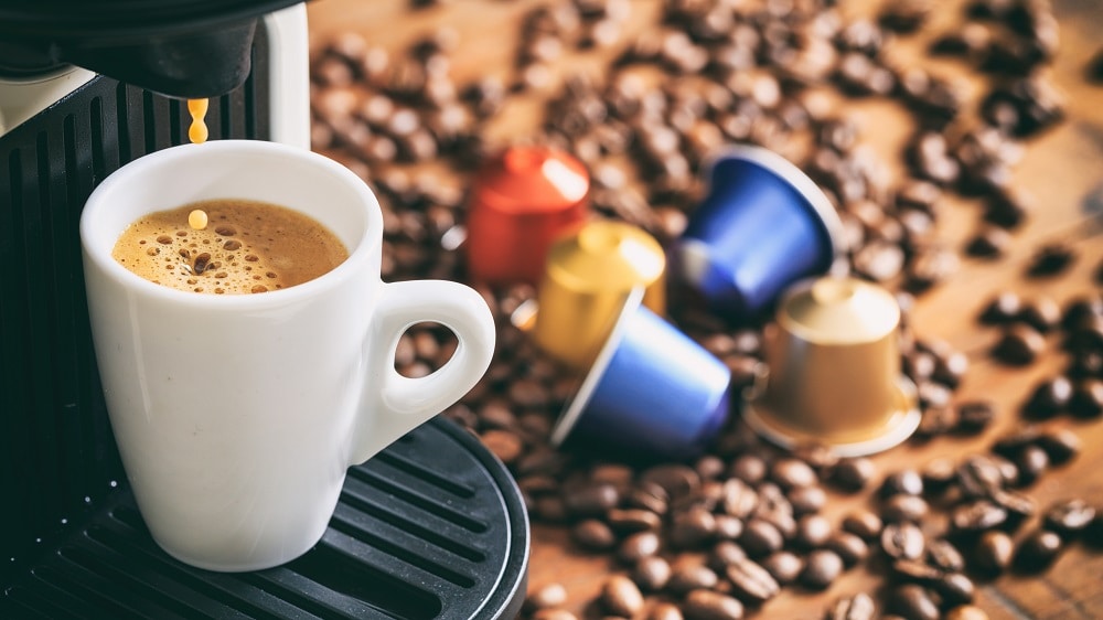 Een koffiecupmachine zet een bakje koffie met op de achtergrond koffiecups en koffiebonen