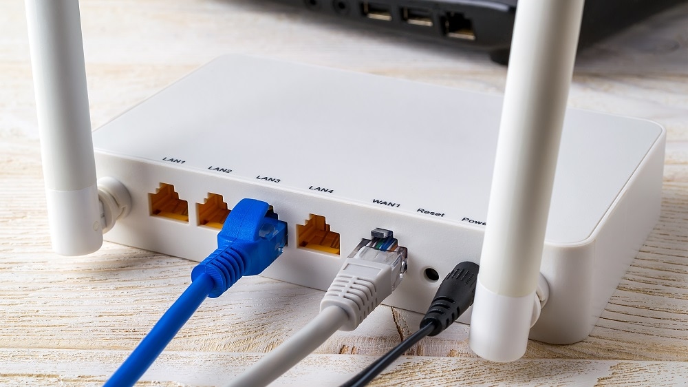 Close-up van netwerkkabels die aan een witte draadloze Wlan-router aangesloten zijn dichtbij laptop op een witte houten ondergrond.