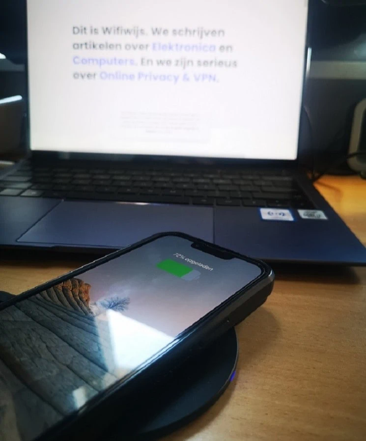 Close-up van een smartphone op een draadloze oplader voor een laptop waarop de website van Wifiwijs geopend is