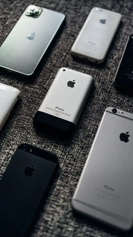 Meerdere verschillende iPhone-modellen naast- en bovenelkaar neergelegd op een grijze, stoffen ondergrond