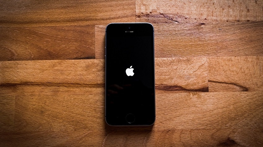Een zwarte Apple iPhone met een zwart scherm met daarin het Apple-logo ligt op een houten ondergrond