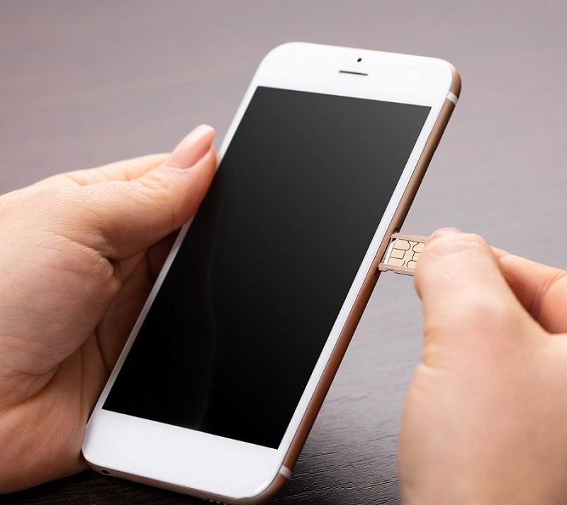 Een iPhone met een open simtray met daarin een simkaart in de handen van een vrouw