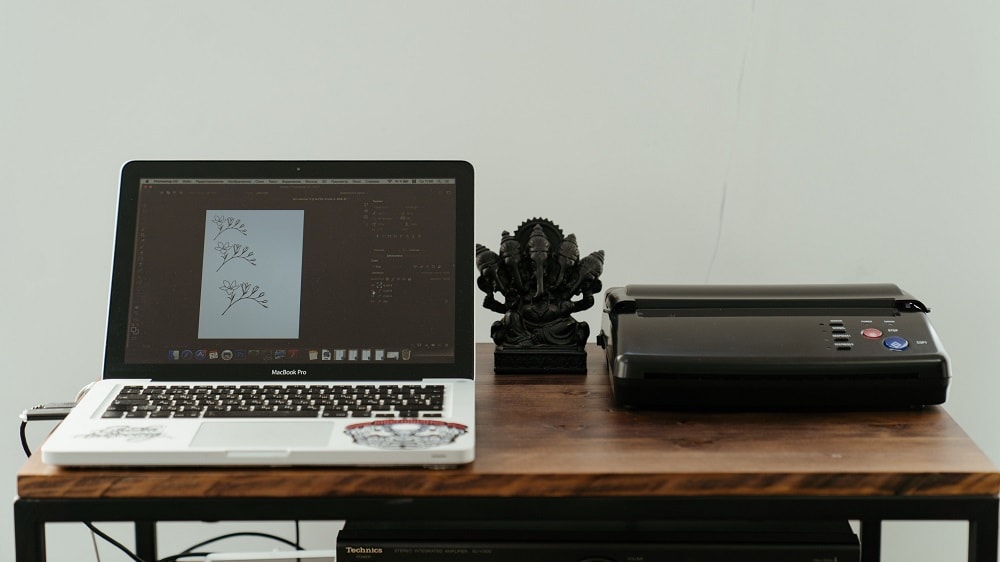 Witte laptop op een houten bureau is verbonden met een zwarte printer die ernaast staat