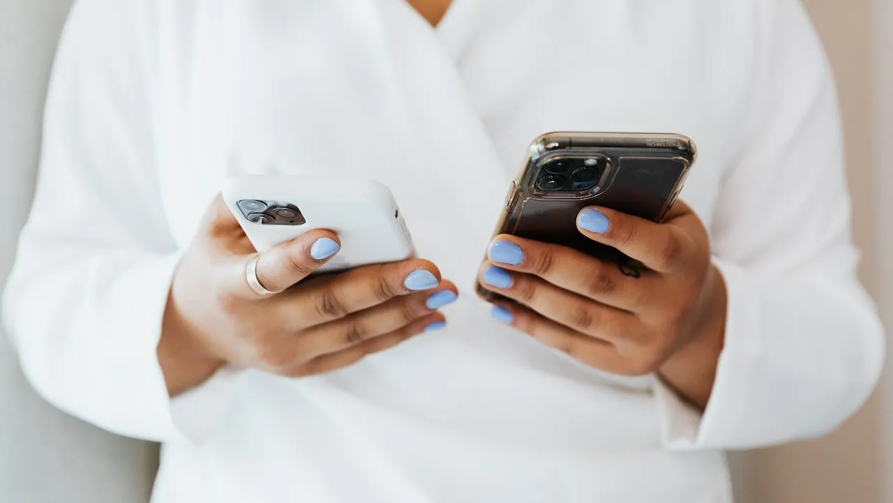 persoon in witte bloes houdt met gelakte nagels twee iphones vast