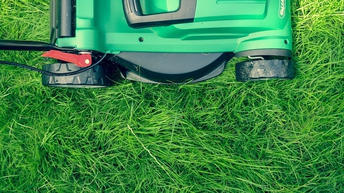 Bovenaanzicht van een groene elektrische grasmaaier met een cirkelmaaitechniek op een ondergrond met lang gras