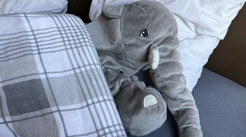 Grijze olifantenknuffel in bed onder een geruite deken