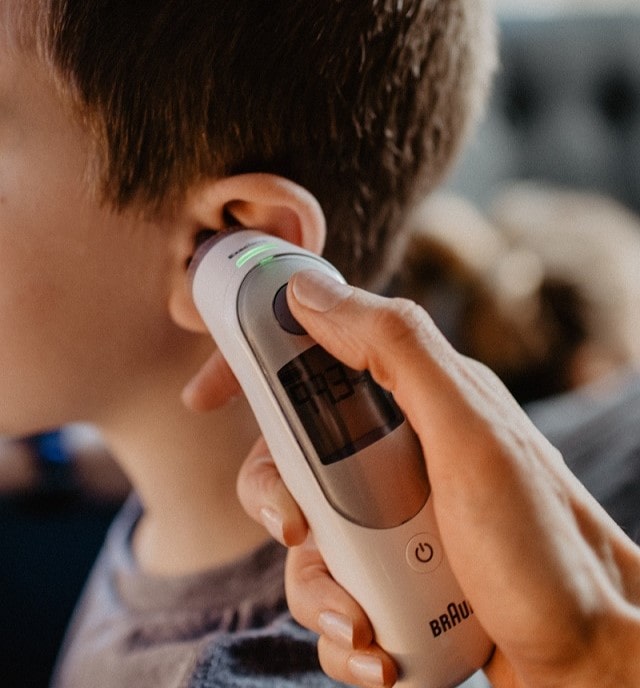Iemand gebruikt een oorthermometer om de lichaamstemperatuur van een kind te meten