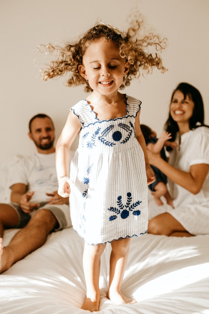 Jong meisje springt blij op het bed van haar ouders terwijl haar ouders lachend toekijken