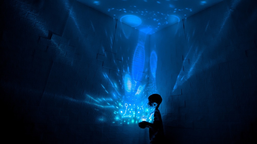 Kleine jonge heeft een lamp in zijn handen die met blauw licht vormpjes projecteert op de muren om hem heen