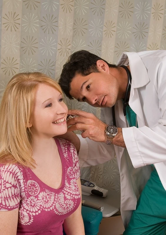 Mannelijke arts doet een meting in het oor van een lachende vrouw