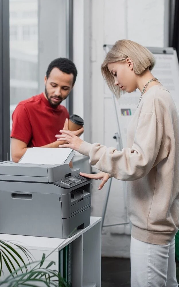Vrouw gebruikt een grijze printer en daarachter staat een glimlachende man