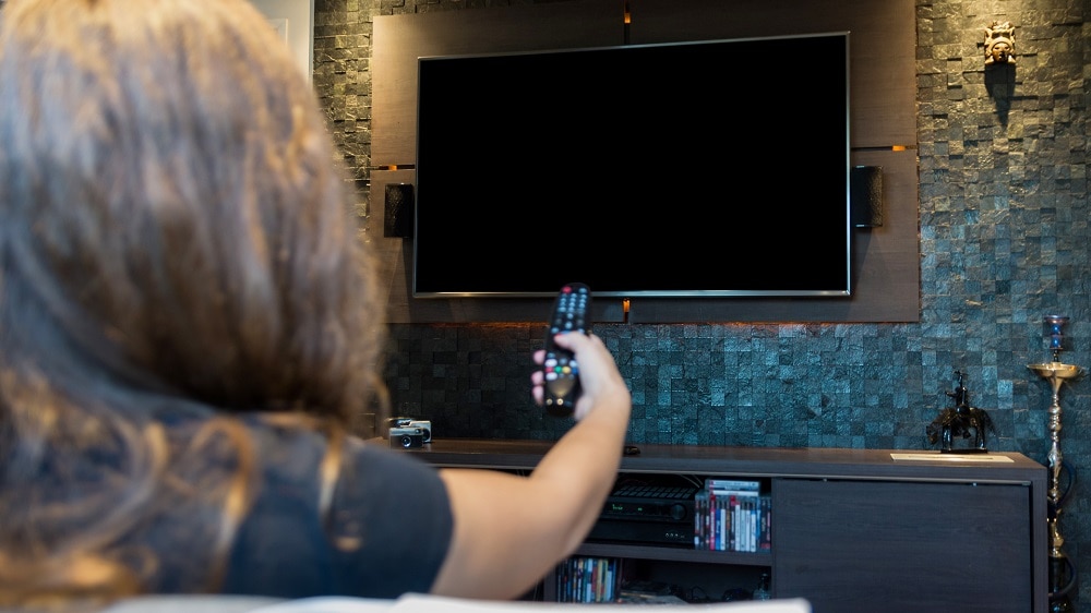 Vrouw wijst met de afstandsbediening naar de tv aan de muur die nog uitstaat
