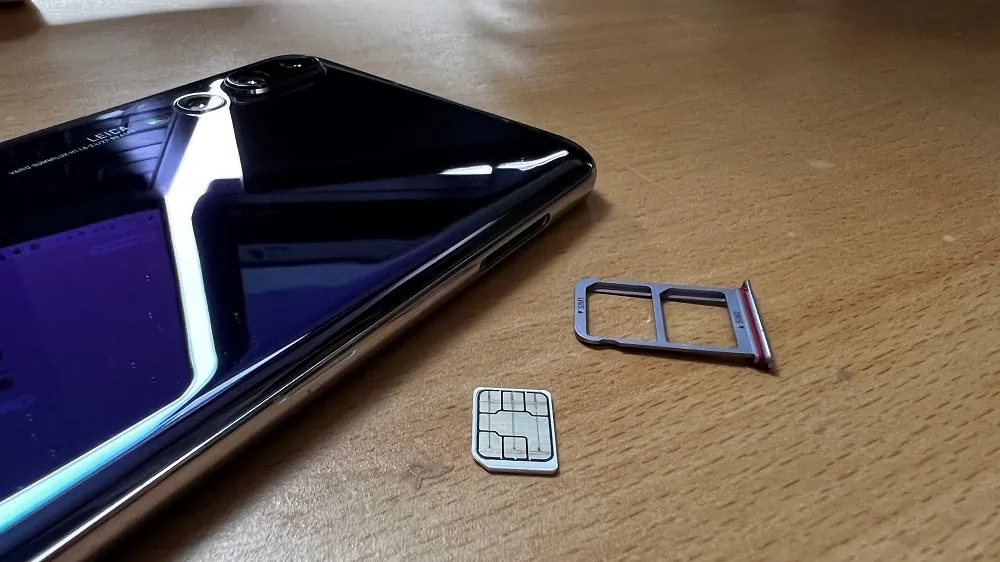 Simkaartje met de chip naar de bovenzijde ligt op een houten ondergrond naast een simtray met daarachter een smartphone