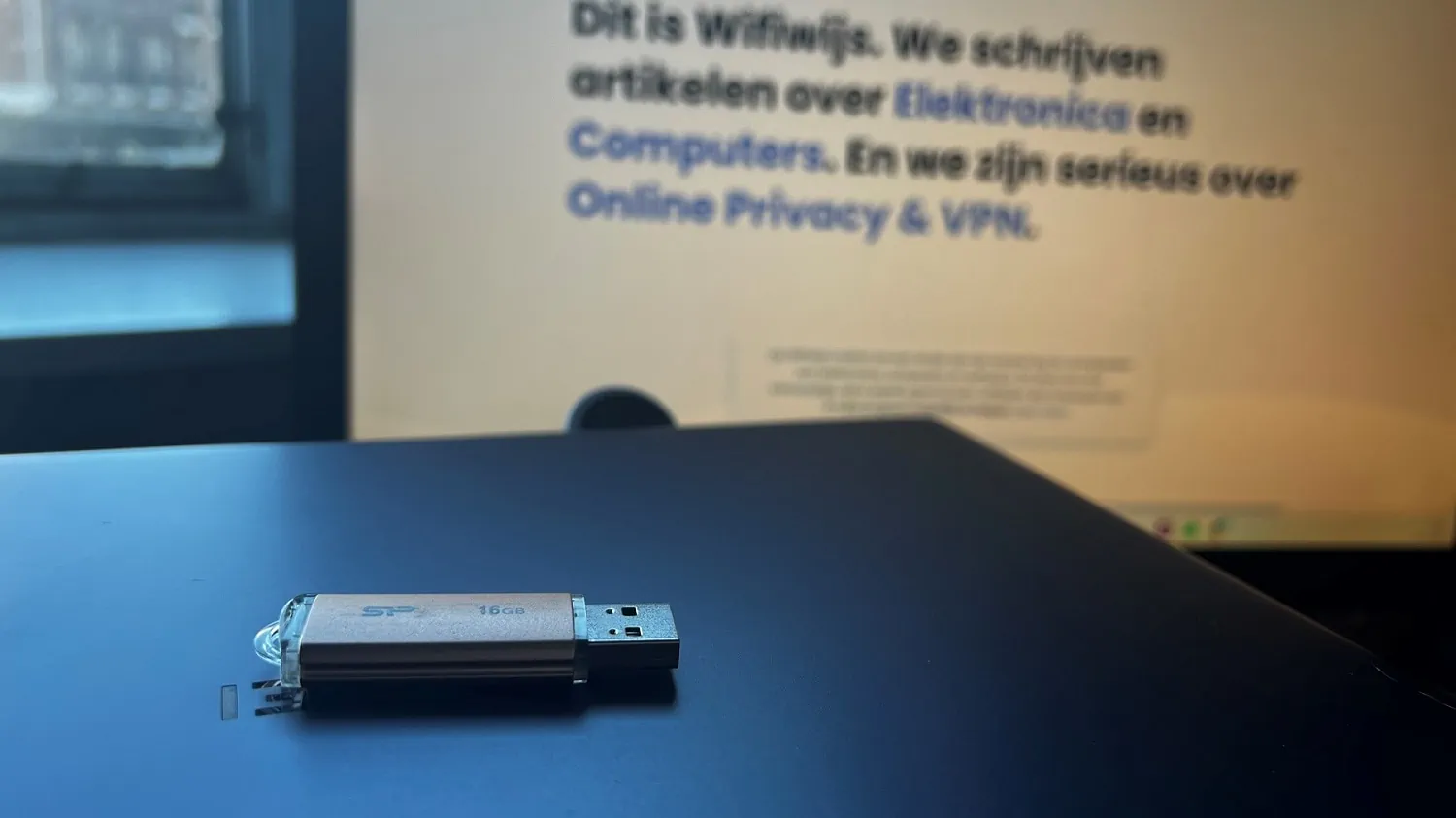 Usb-stick op een dichtgeklapte laptop met op de achtergrond een monitor met daarop de site van Wifiwijs geopend