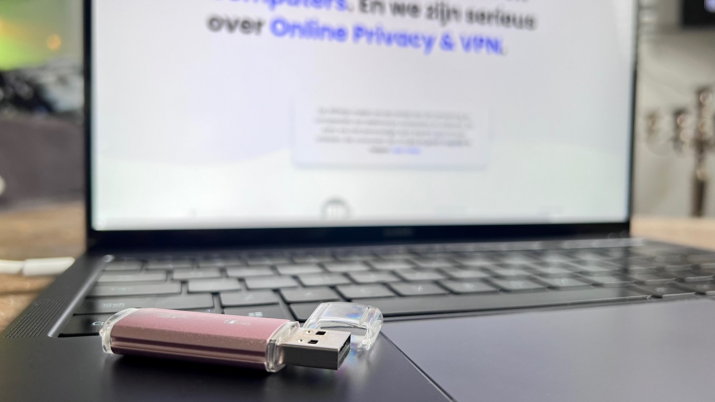 Close-up van een roze usb-stick naast de touchpad van een laptop waarop de website van Wifiwijs is geopend