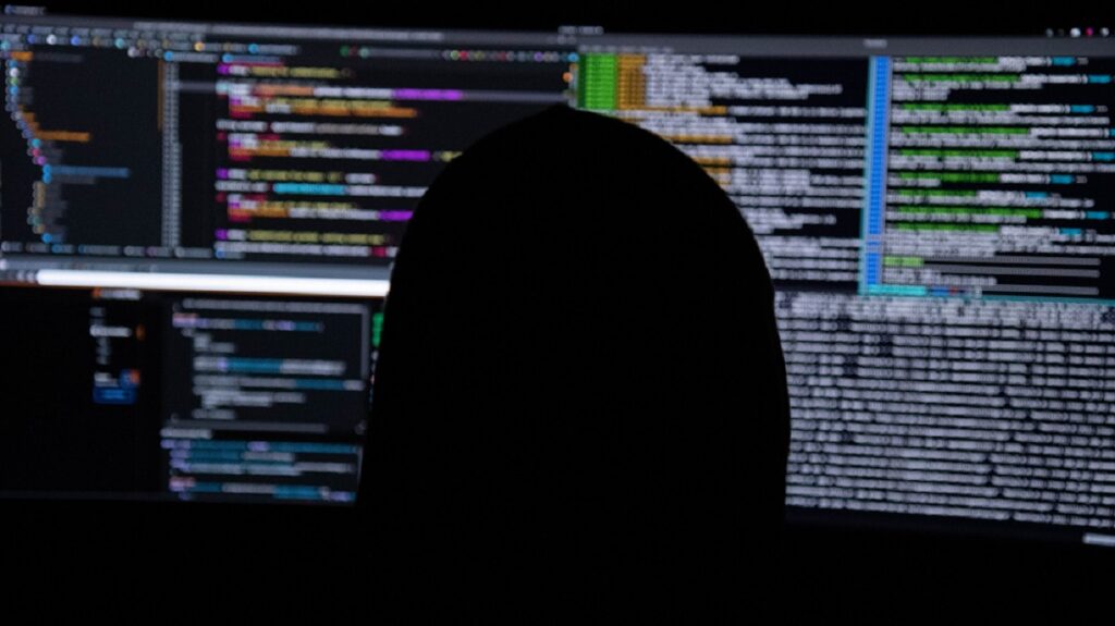 Donkere silhouet van iemand achter een monitor met allerlei codes erop