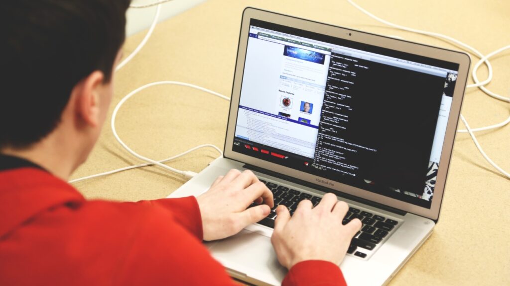 Man in rode trui voert een code in op een MacBook 