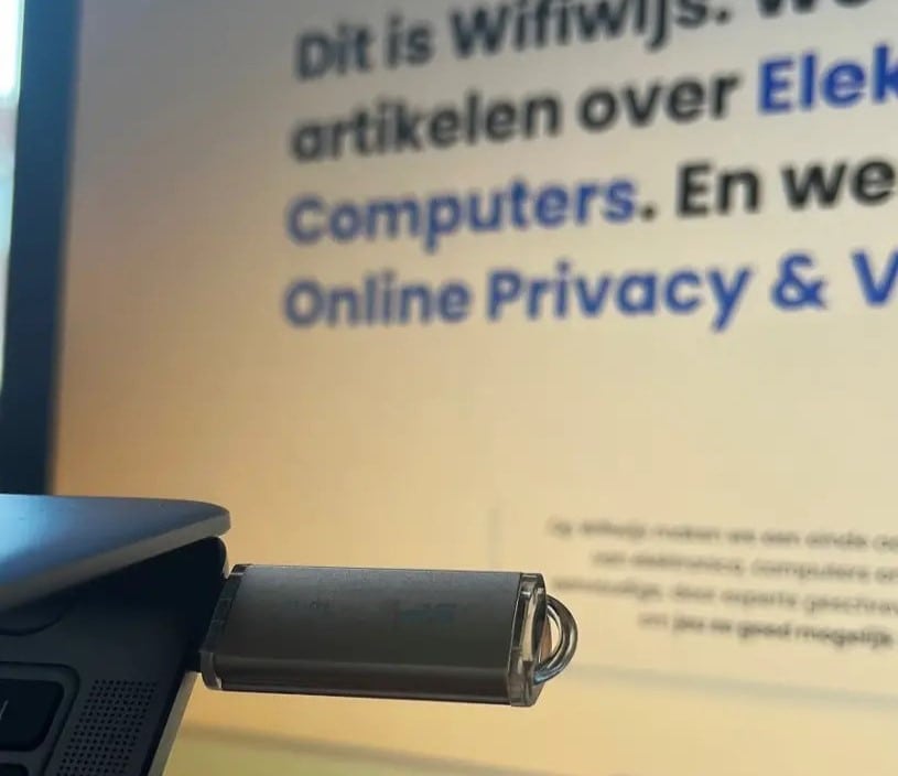 Usb-stick in de usb-poort van een laptop met op de achtergrond een monitor met daarop de site van Wifiwijs geopend