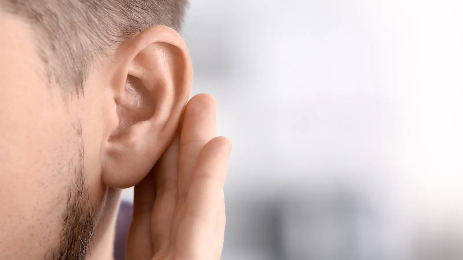 Close-up van een oor van een man met daarachter een hand om het beter te kunnen horen